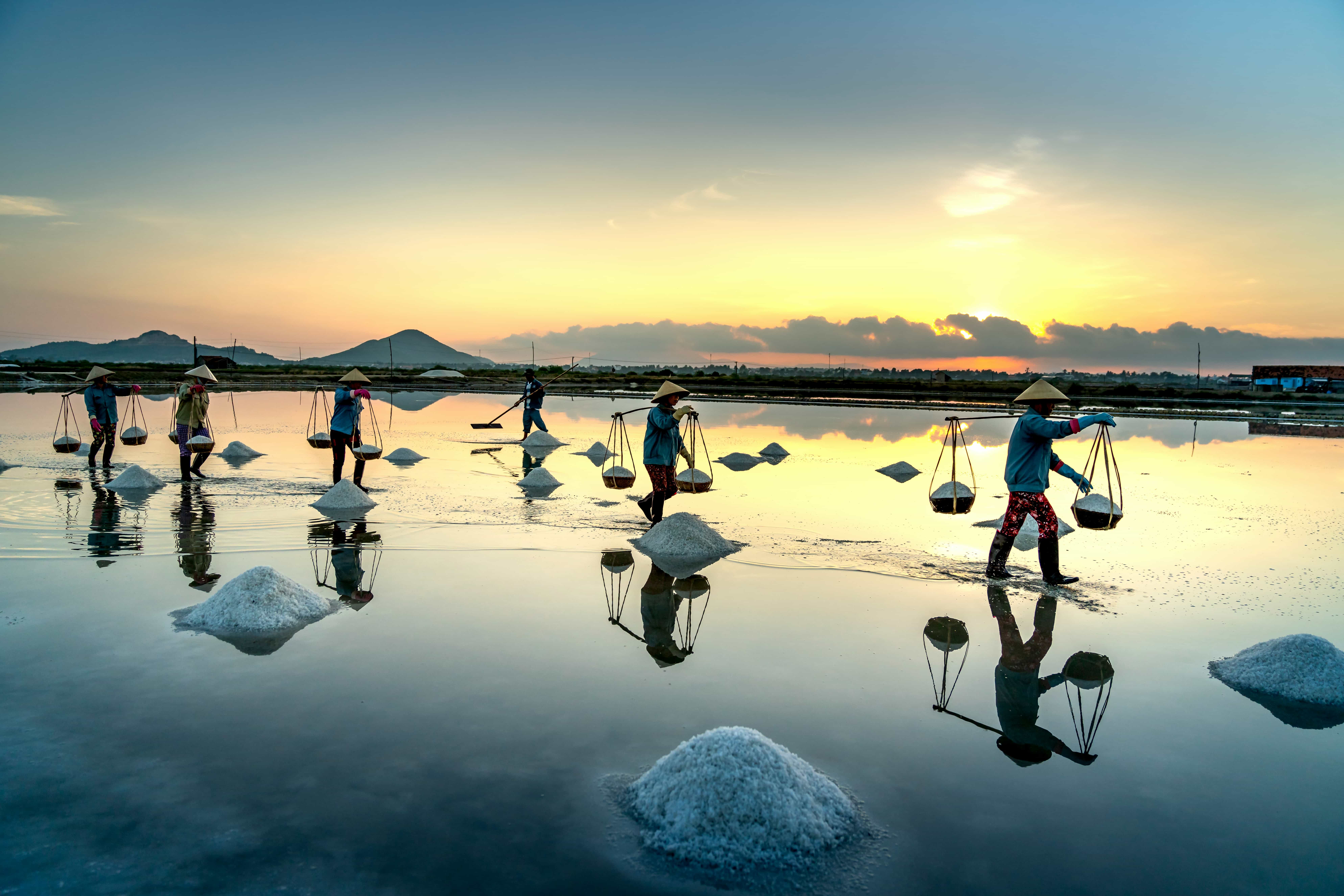 Salt pan harvest at golden hour with worker silhouette